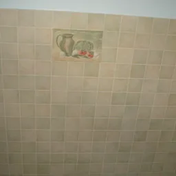 Ściana wyłożona jasnymi, kwadratowymi płytkami ceramicznymi z dekoracyjnym panelem przedstawiającym dzban i warzywa, przy której widać dłoń z nożem do cięcia płytek.